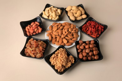 Bowls with dried fruits and nuts on beige background