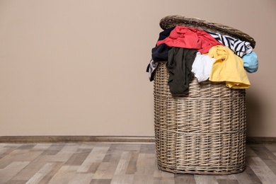 Photo of Laundry basket with dirty clothes on floor indoors. Space for text