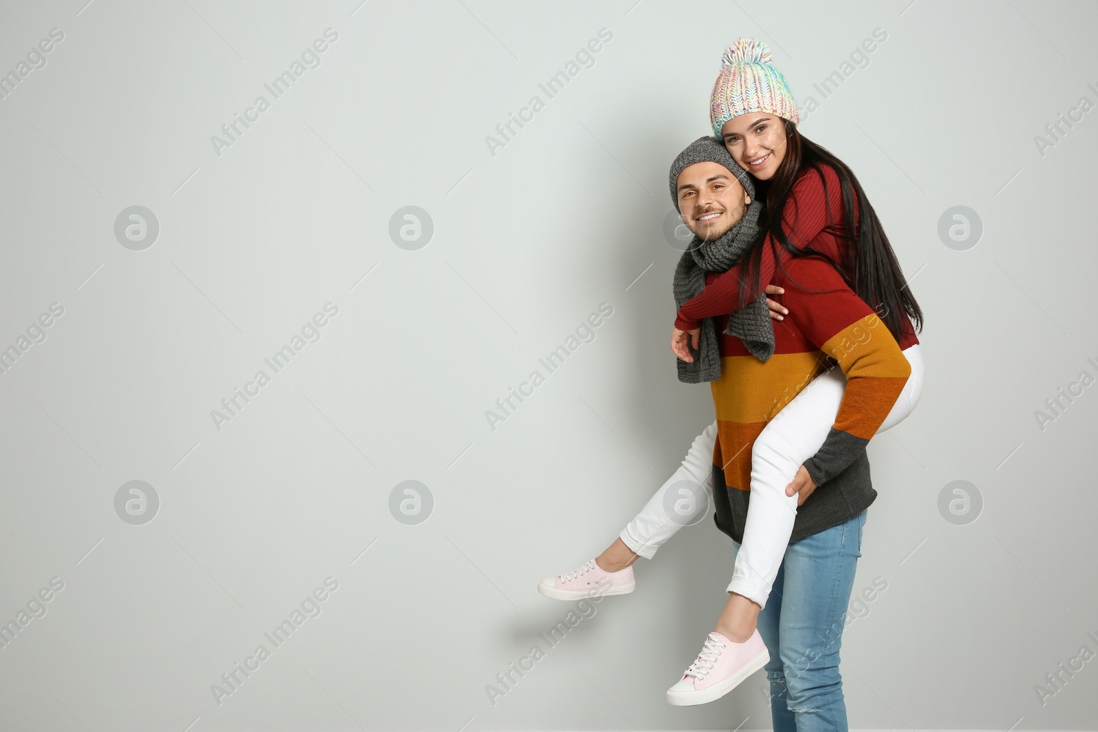 Photo of Young happy couple in warm clothes on light background. Christmas celebration