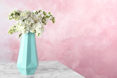 Photo of Blossoming lilac flowers in vase on marble table against color background. Space for text