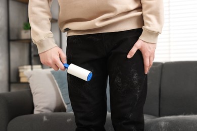 Photo of Pet shedding. Man with lint roller removing dog's hair from pants at home, closeup