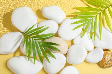 Photo of Spa stones and palm leaves in water on yellow background, flat lay