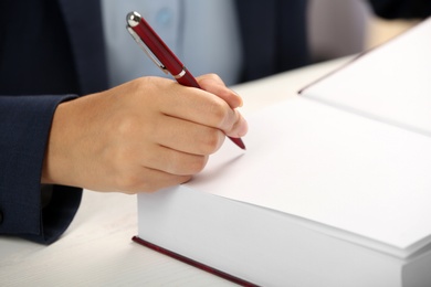 Photo of Writer signing autograph in book at table, closeup