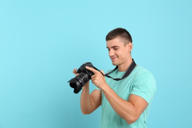 Photo of Young photographer with professional camera on light blue background. Space for text