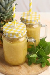 Photo of Tasty pineapple smoothie in mason jars, mint and fruit on table, closeup