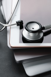 Stack of electronic devices and stethoscope on black table, closeup