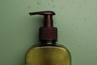 Photo of Bottle of face cleansing product on green background, top view