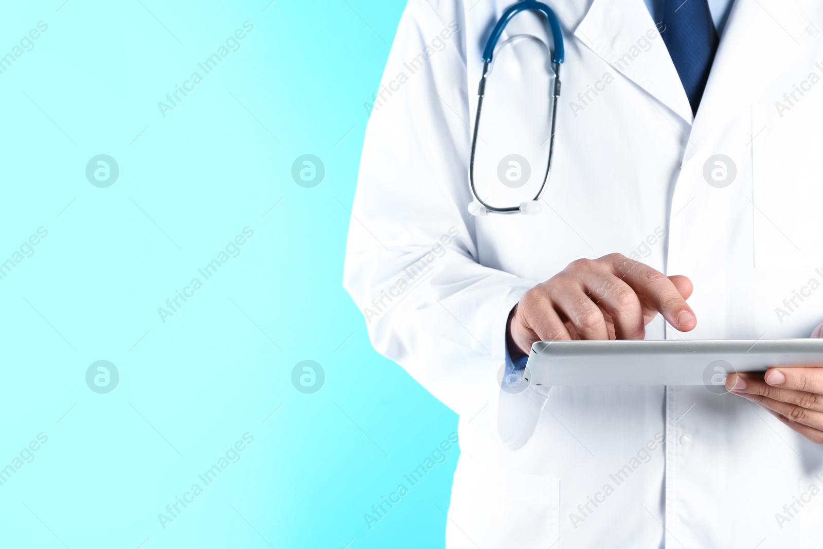 Photo of Male doctor holding modern tablet on color background, closeup with space for text