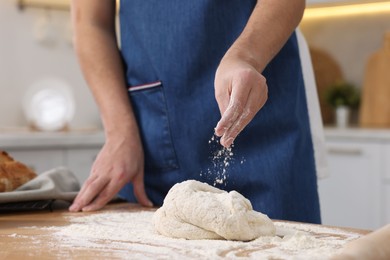 Making bread. Man sprinkling flour onto dough at wooden table in kitchen, closeup