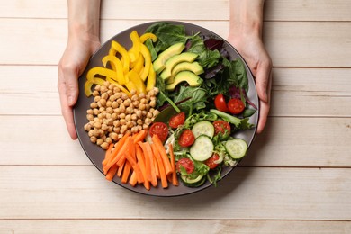 Photo of Balanced diet and vegetarian foods. Woman holding plate with different delicious products at wooden table, top view