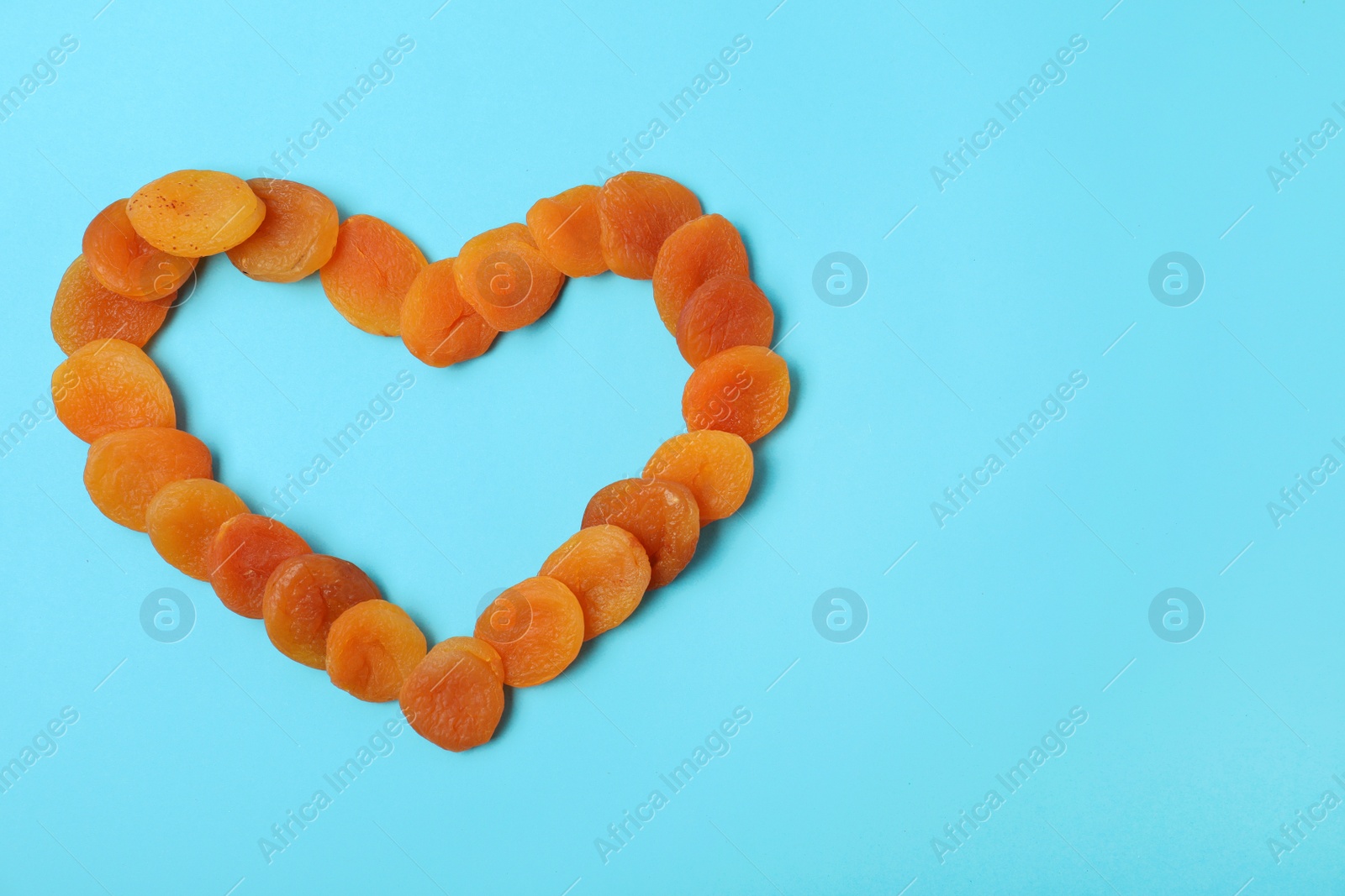 Photo of Heart shaped frame made of dried apricots on color background, top view with space for text. Healthy fruit