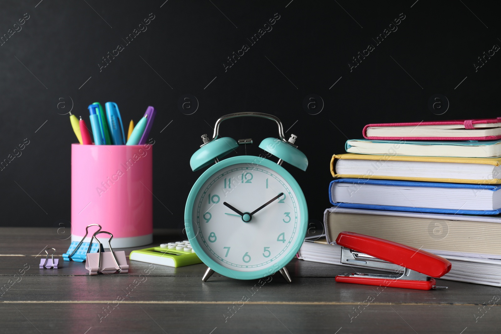 Photo of Alarm clock and different stationery on wooden table near blackboard. School time