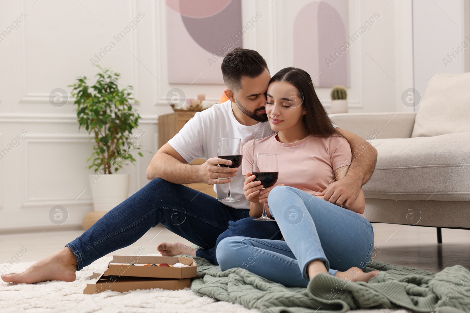 Photo of Affectionate young couple eating pizza and drinking wine at home