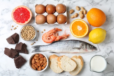 Flat lay composition of different products on white marble table. Food allergy concept