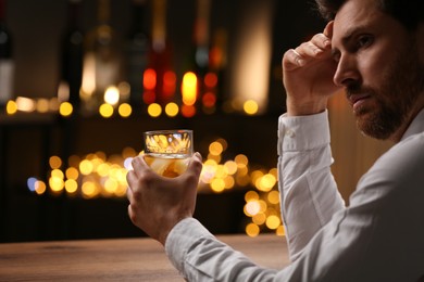 Man with glass of whiskey at bar counter against blurred lights. Space for text