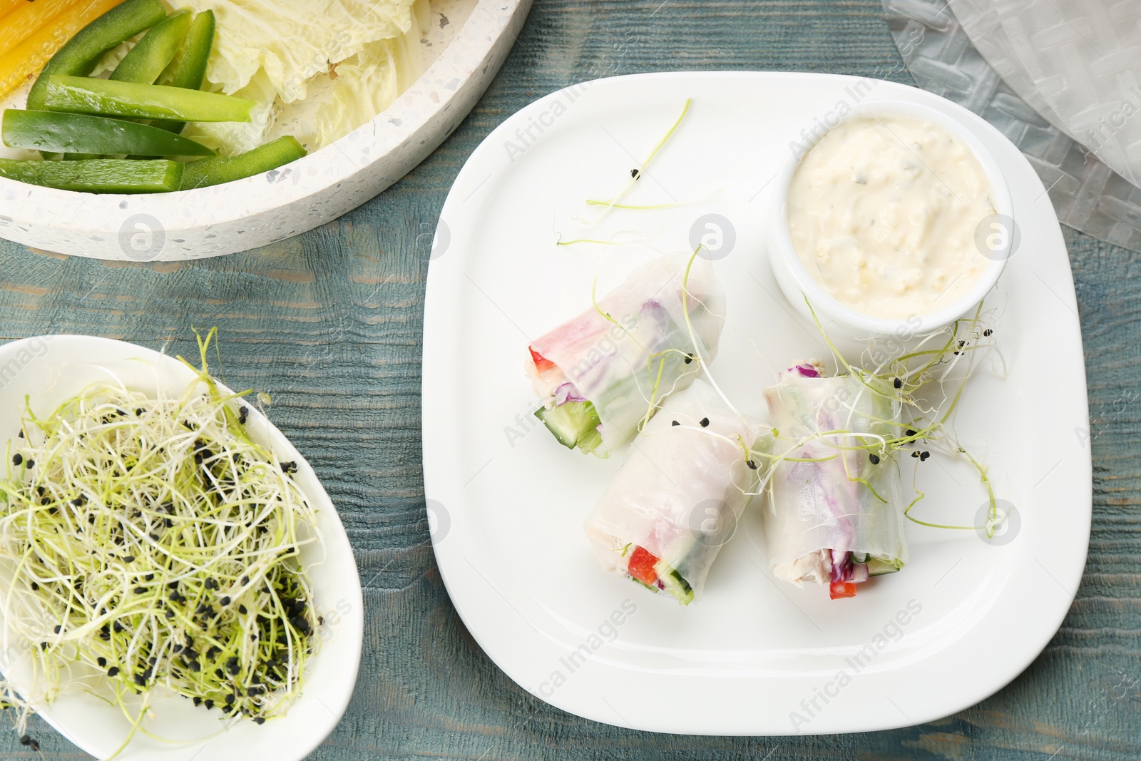 Photo of Delicious rolls wrapped in rice paper on light blue wooden table, flat lay