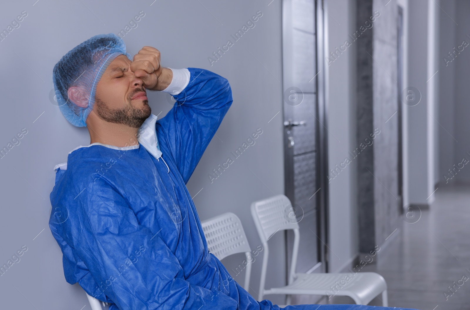 Photo of Exhausted doctor sitting on chair in hospital corridor, space for text