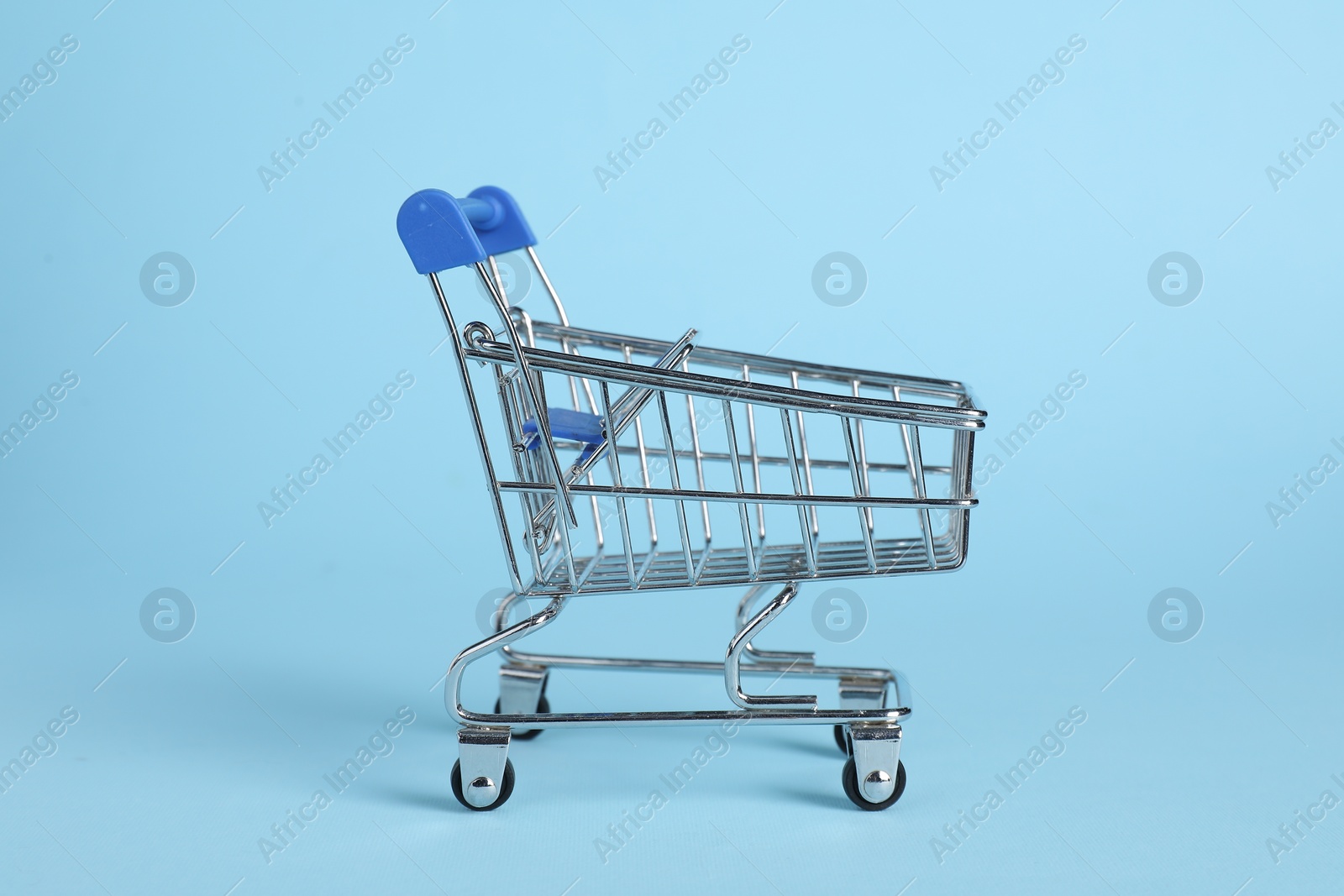 Photo of Small metal shopping cart on light blue background