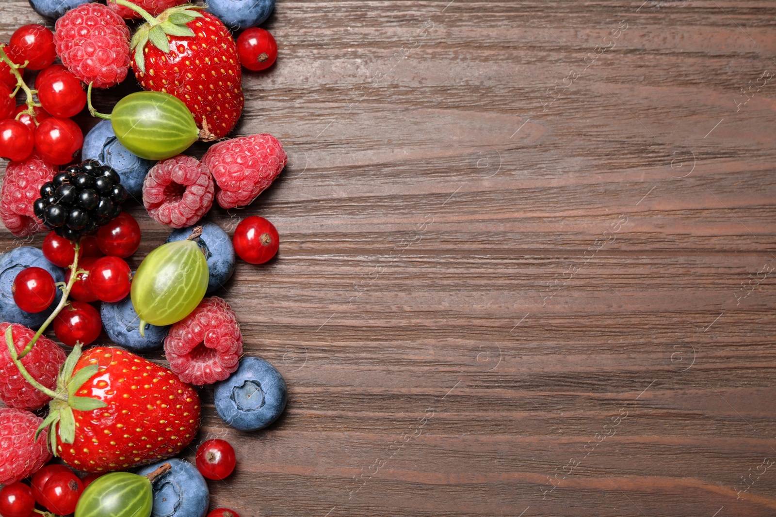 Photo of Different fresh berries on wooden table, flat lay. Space for text