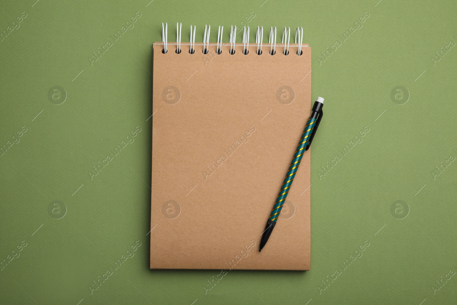 Photo of Kraft notebook and pencil on green background, top view