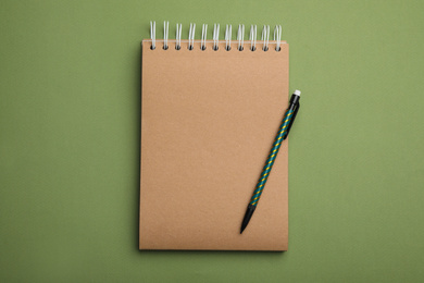 Photo of Kraft notebook and pencil on green background, top view