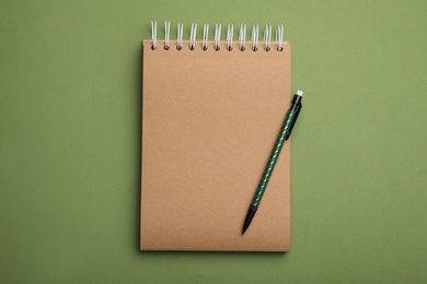 Kraft notebook and pencil on green background, top view