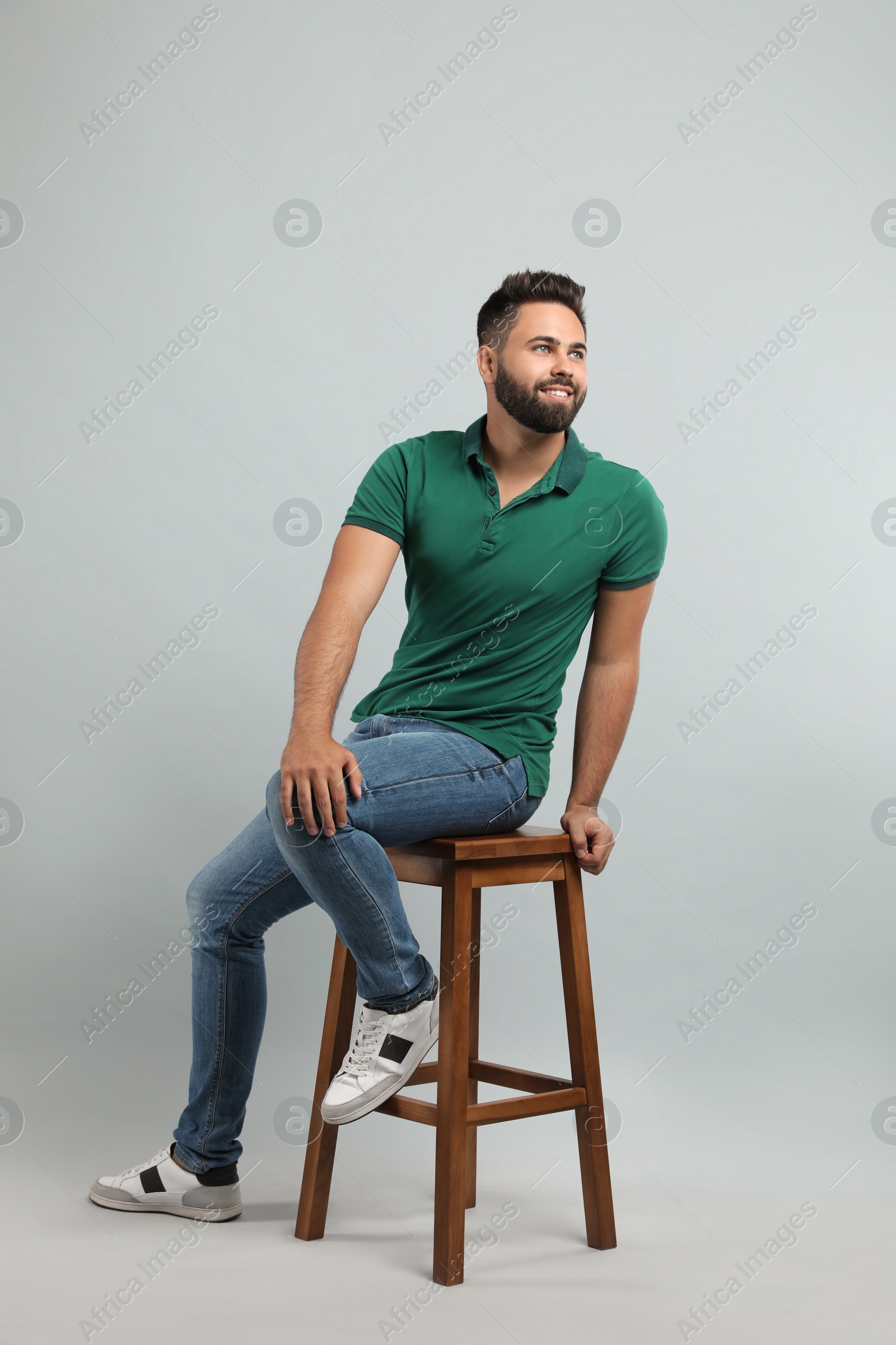 Photo of Handsome young man sitting on stool against light grey background