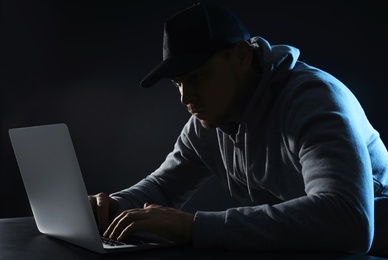 Photo of Man using laptop at table on dark background. Criminal activity