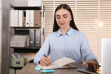 Happy woman taking notes at wooden table in office