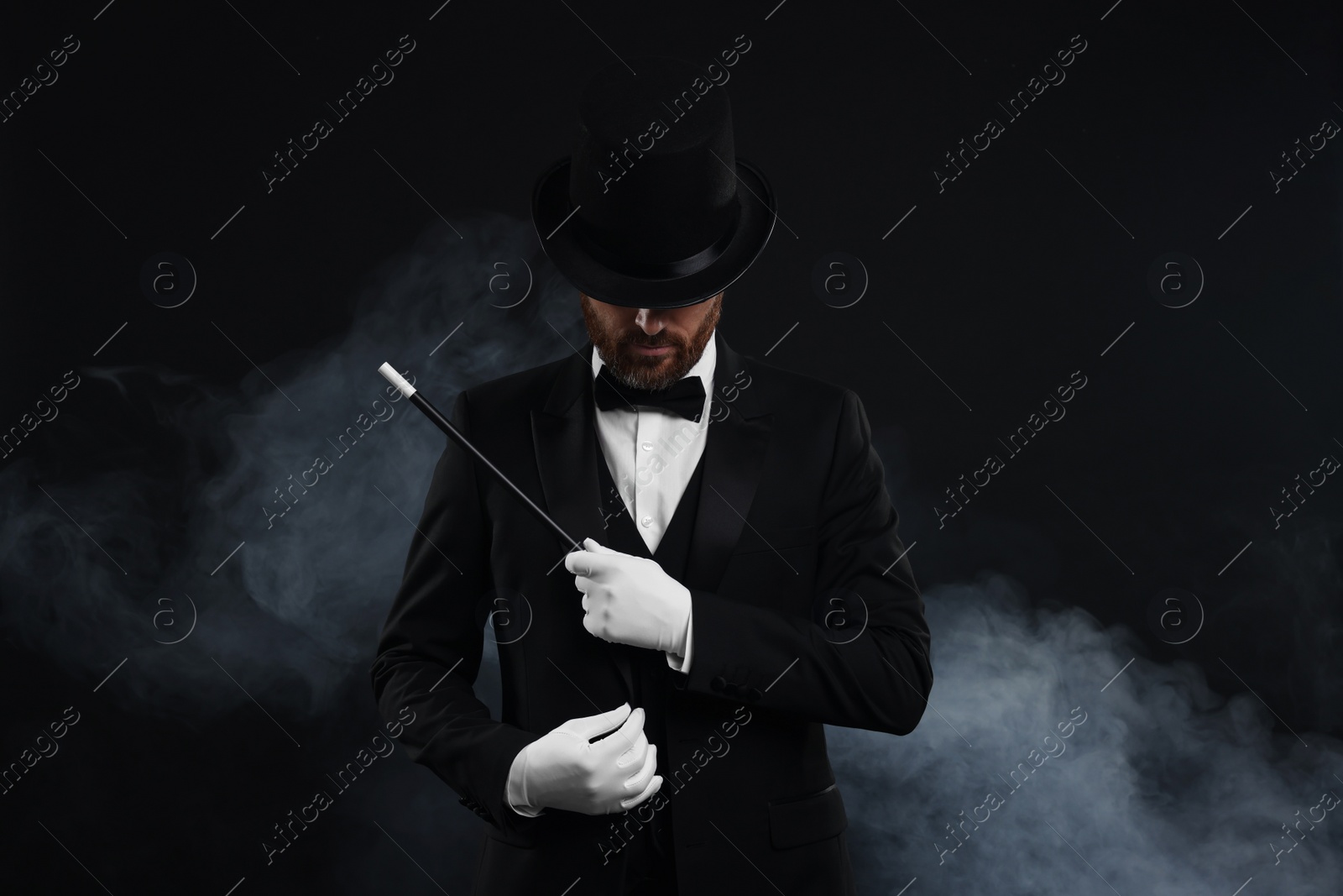 Photo of Magician holding wand in smoke on black background