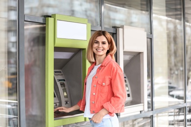 Beautiful woman using cash machine for money withdrawal outdoors