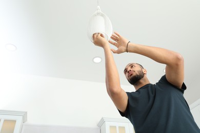 Photo of Young man repairing ceiling lamp indoors, low angle view. Space for text
