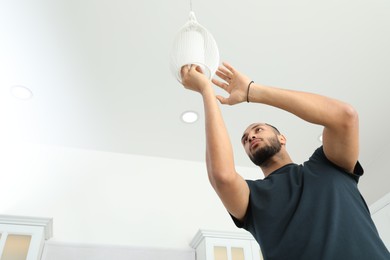 Young man repairing ceiling lamp indoors, low angle view. Space for text