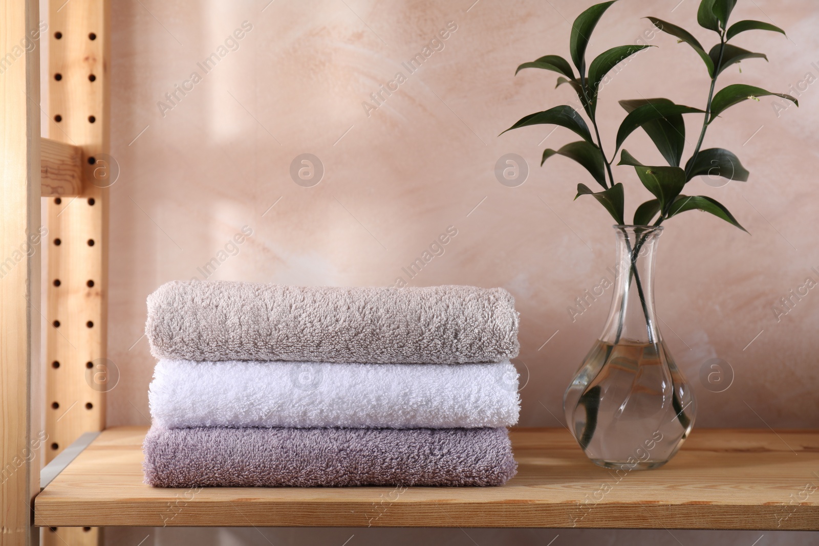 Photo of Stacked soft towels and green leaves on wooden shelf indoors