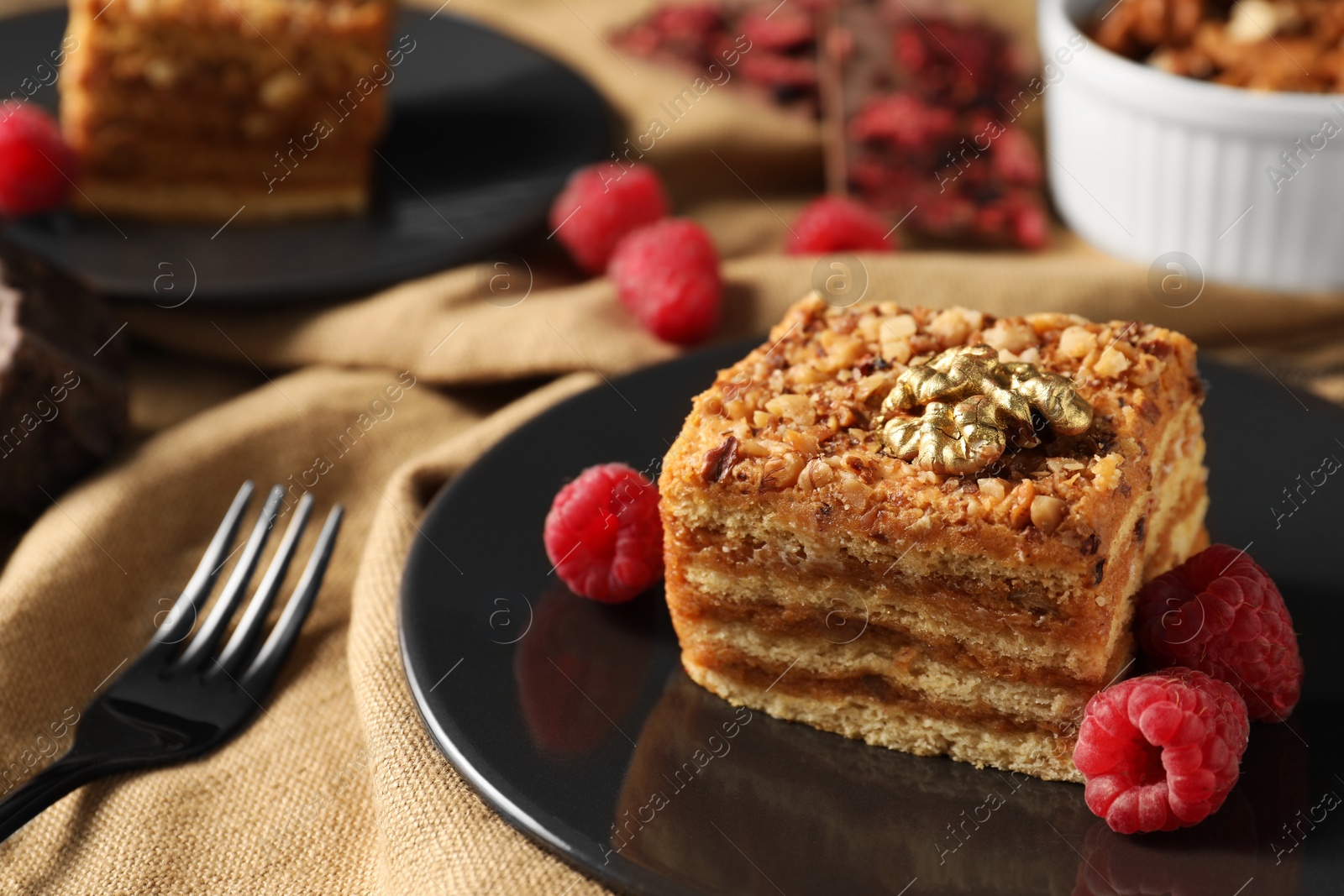 Photo of Pieces of delicious layered honey cake with nuts and raspberries served on table, closeup. Space for text