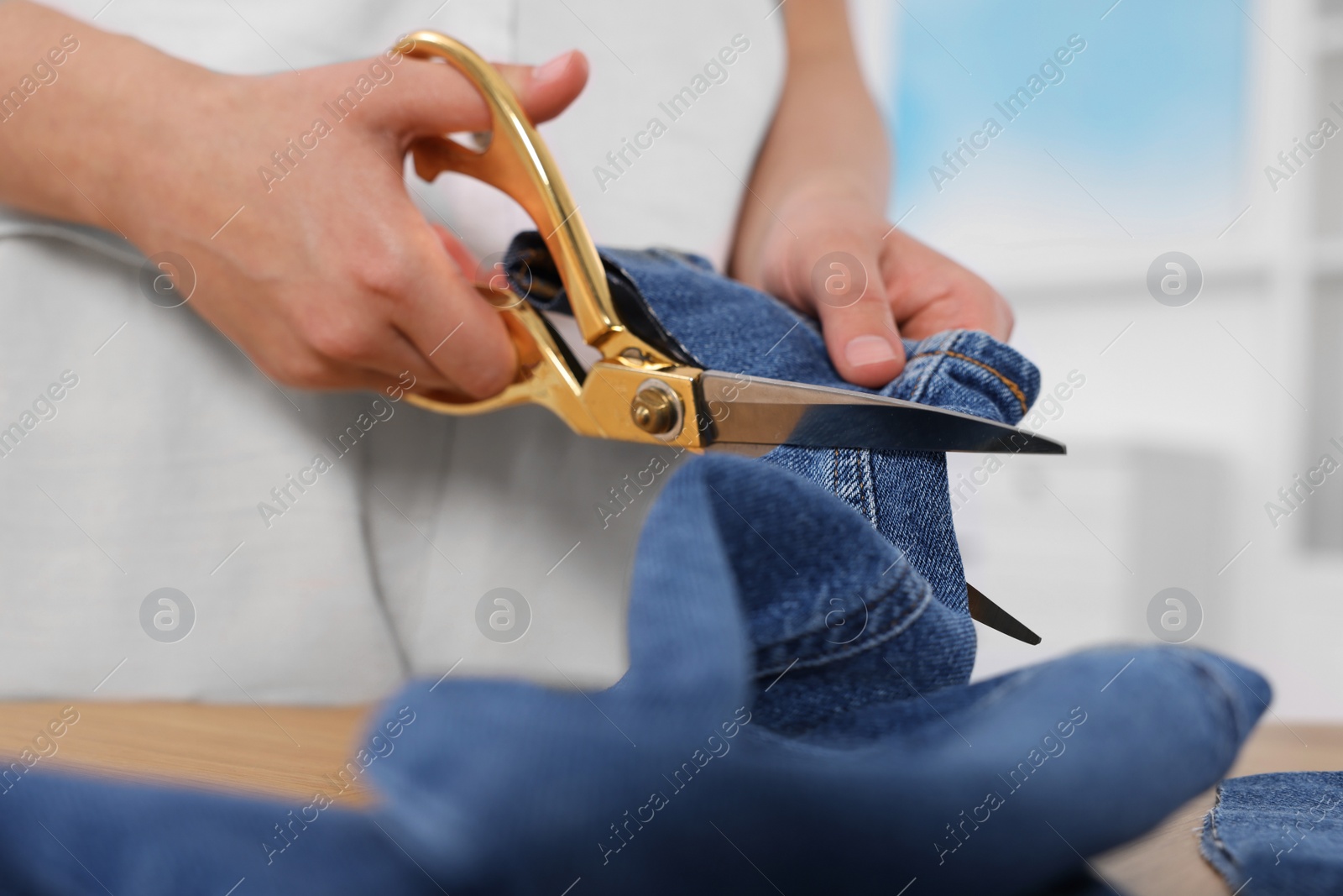 Photo of Woman cutting hem of jeans at table, closeup