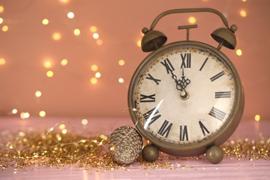 Photo of Vintage clock with decor on pink table against blurred Christmas lights, closeup. New Year countdown