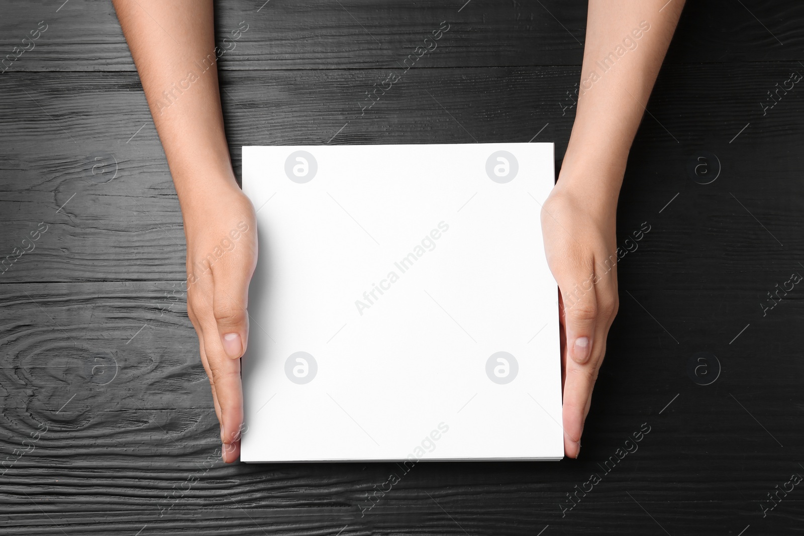 Photo of Woman holding blank paper sheets for brochure at black wooden table, top view. Mock up