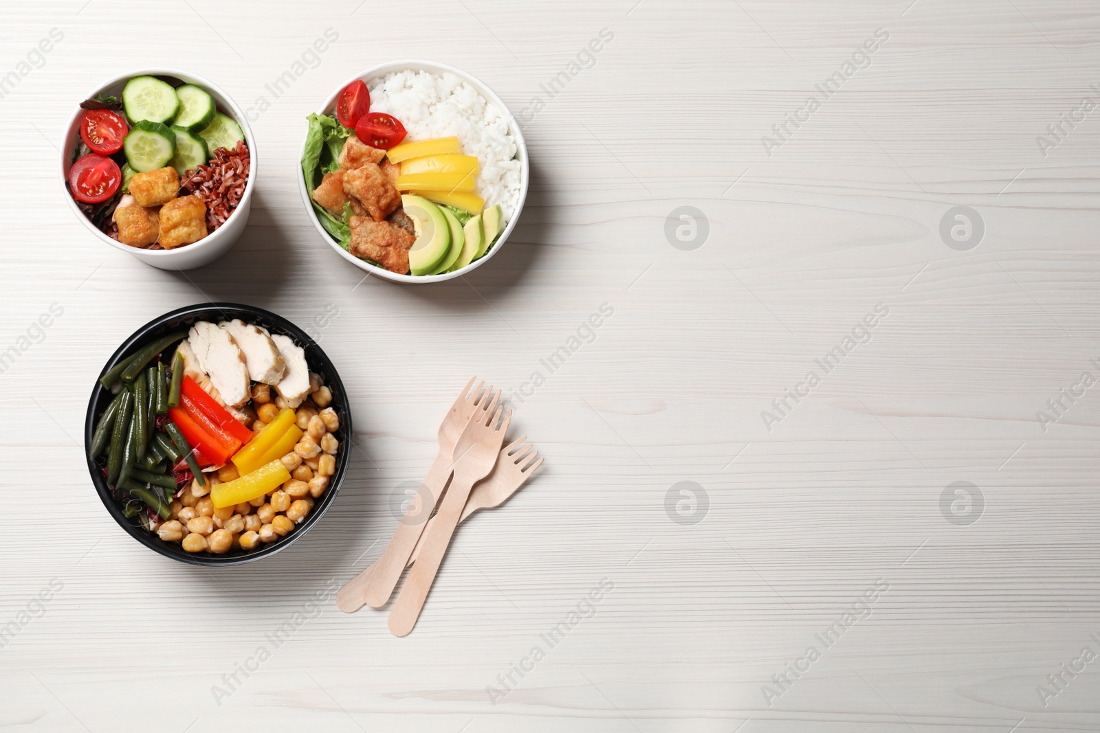 Photo of Different healthy meals in takeaway containers and wooden forks on white table, flat lay. Space for text