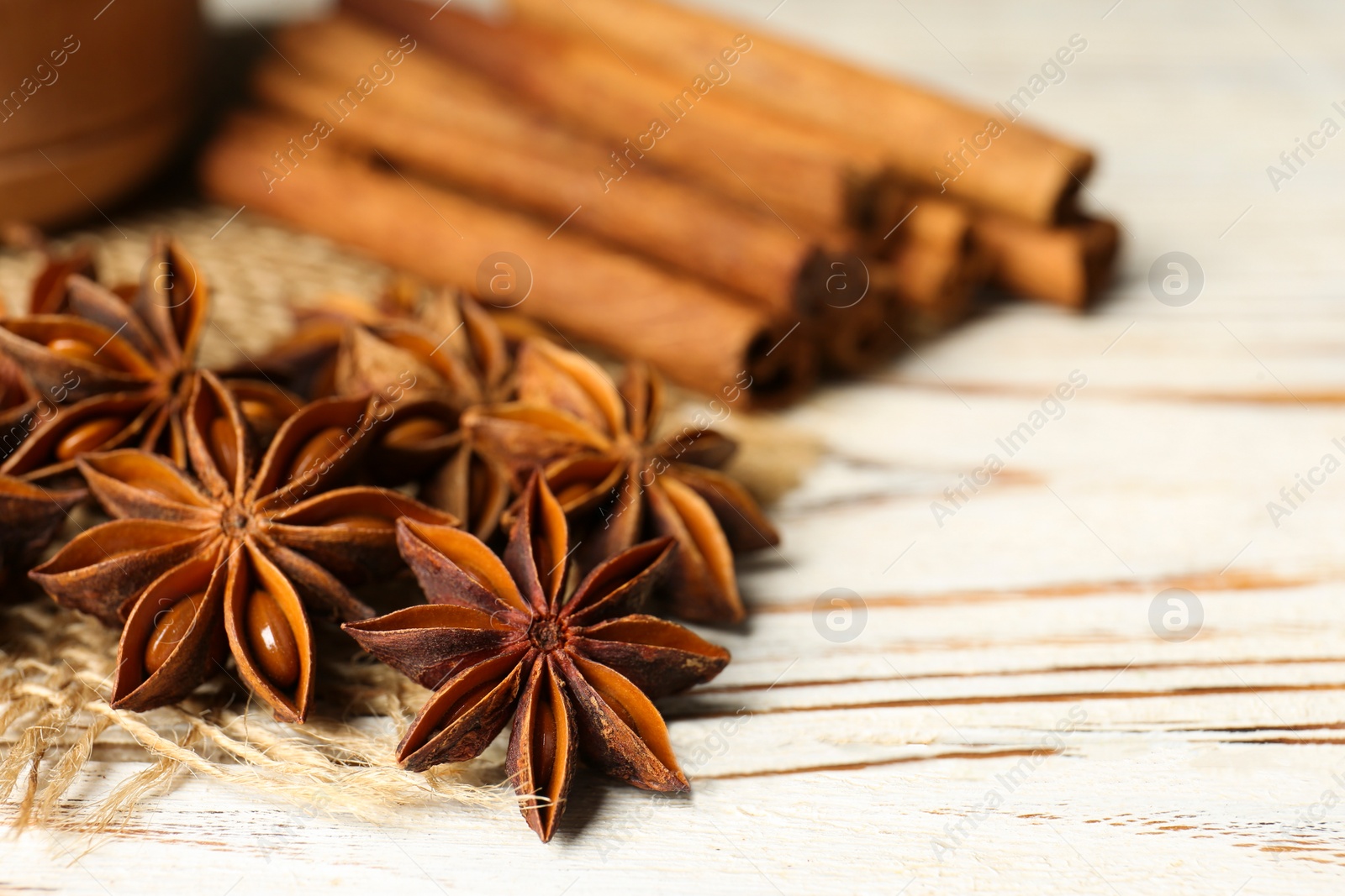 Photo of Many aromatic anise stars and cinnamon sticks on white wooden table, closeup