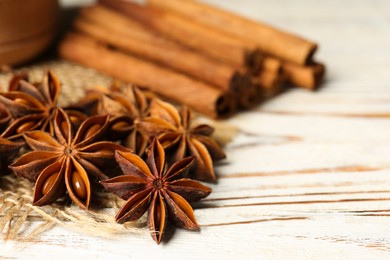 Photo of Many aromatic anise stars and cinnamon sticks on white wooden table, closeup