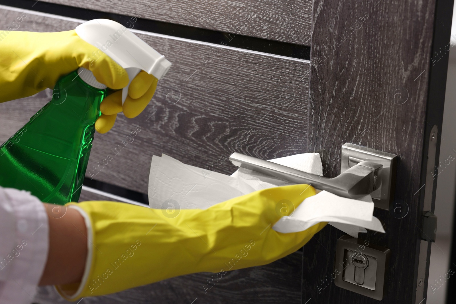 Photo of Woman cleaning door handle with detergent and paper towel, closeup