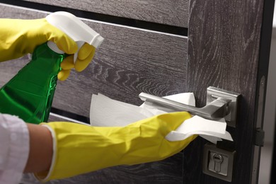 Woman cleaning door handle with detergent and paper towel, closeup