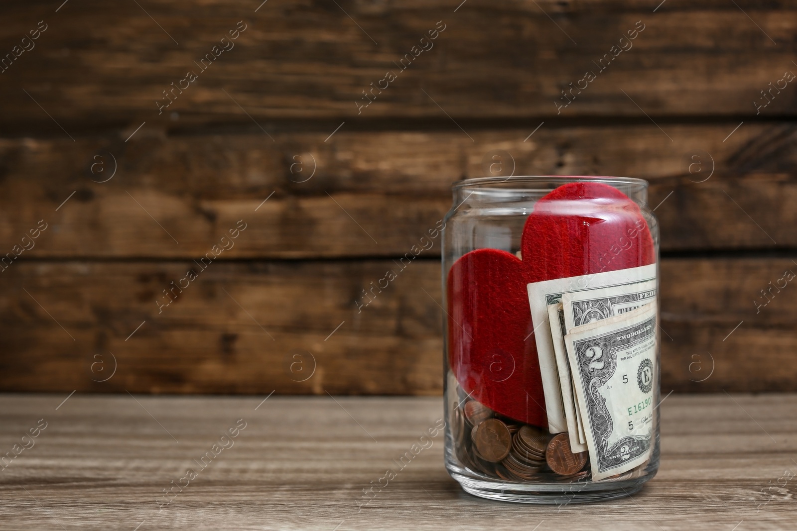 Photo of Donation jar with money and red heart on table. Space for text