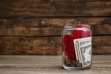 Photo of Donation jar with money and red heart on table. Space for text