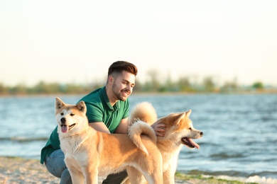 Young man walking his adorable Akita Inu dogs near river