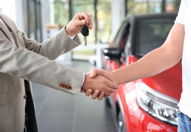 Photo of Salesman shaking hands with customer while giving car key in auto dealership, closeup