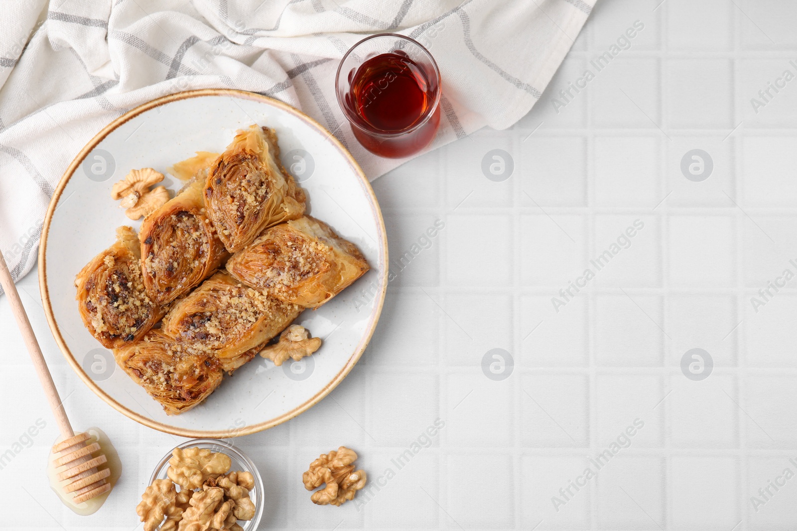 Photo of Eastern sweets. Pieces of tasty baklava, walnuts and tea on white tiled table, flat lay. Space for text