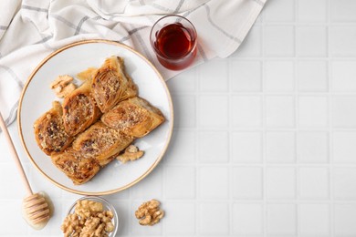 Photo of Eastern sweets. Pieces of tasty baklava, walnuts and tea on white tiled table, flat lay. Space for text