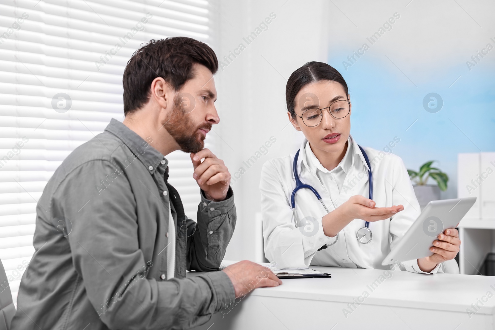 Photo of Doctor with tablet consulting patient during appointment in clinic